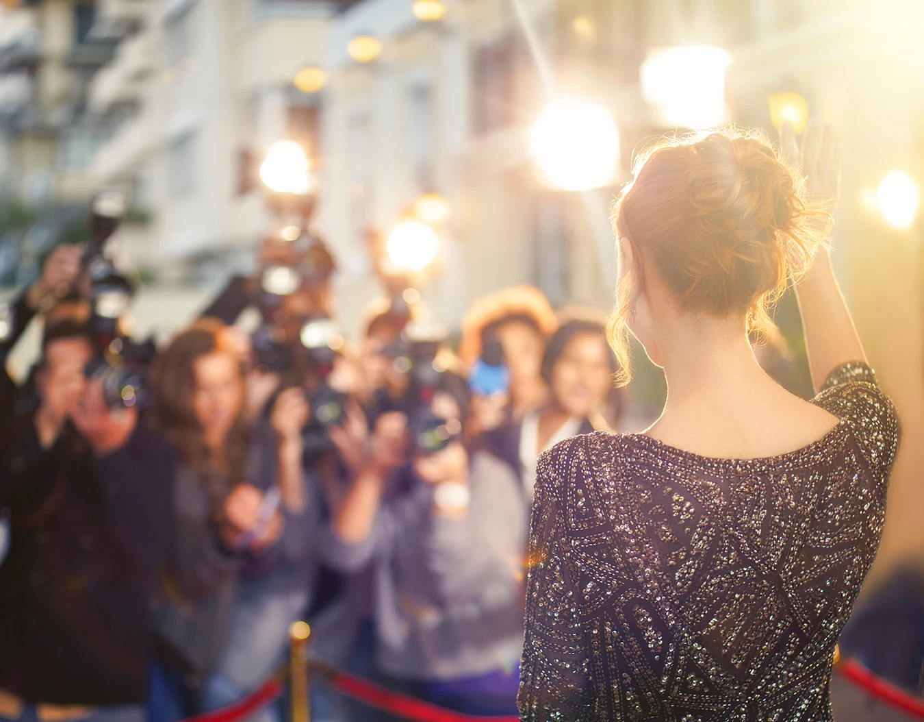 A female celebrity with red hair, in a beautiful black and sequined gown, walking down the red carpet at a Hollywood event, waving at reporters and paparazzi